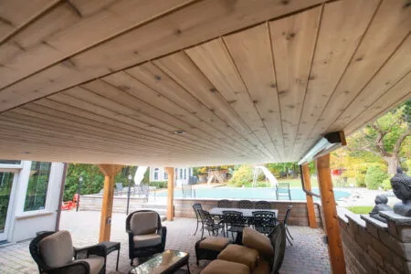 Covered backyard patio with a wood ceiling, seating area, and pool beyond.