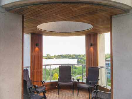 Covered balcony with four wicker chairs, wooden floor and ceiling, overlooking trees and water in the background.