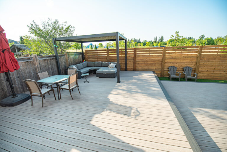 Spacious backyard deck with outdoor furniture, shaded seating area, and wooden privacy fence on a sunny day.